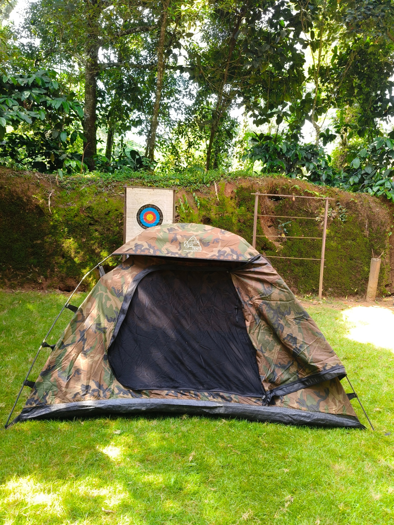 Camouflage adventure tent pitched on grass with archery target behind