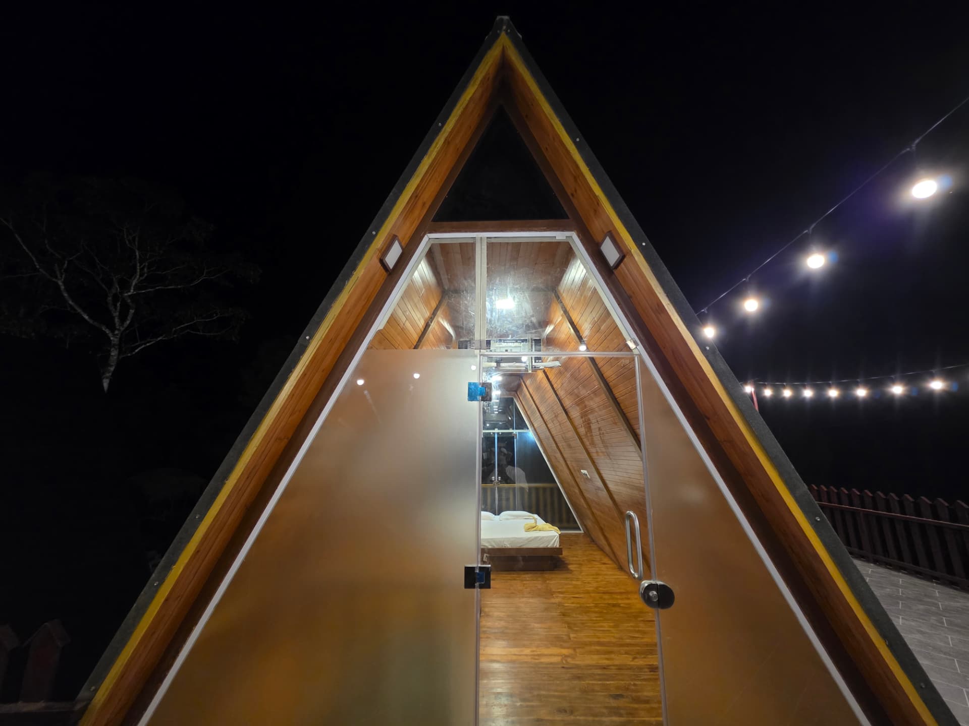 A-Frame cottage glass entrance glowing at night under string lights